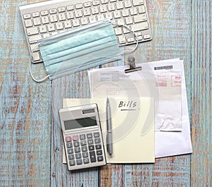 Bills and calculator, and keyboard with face mask on wood table