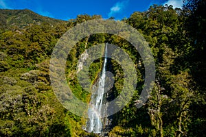 Billy Falls with the Glacial Blue river water flowing over rocks. Haast Pass, South Island, New Zealand