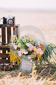 The bin full of colourful flowers is placed near the dark wooden boxes with the camera at the background of the sunny