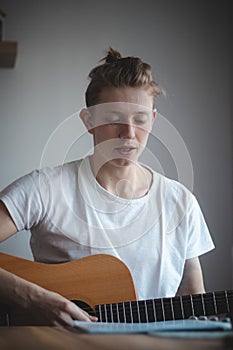 Binary portrait of a new hopeful singer who is leaning on a white wall and holding his favorite instrument and looking into space