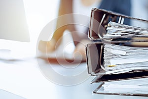 Binders with papers are waiting to be processed by business woman or bookkeeper working at the desk in office back in