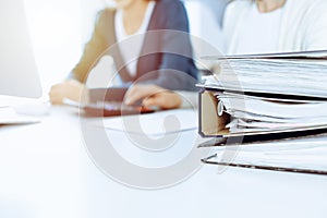 Binders with papers are waiting to be processed by business woman or bookkeeper working at the desk in office back in