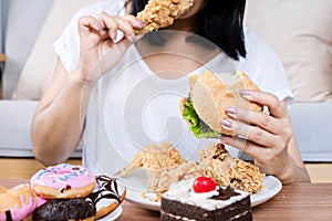 Binge eating disorder concept with woman eating fast food burger, fired chicken , donuts and desserts photo