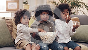 Binging buddies. three adorable little boys eating popcorn and watching movies together at home.