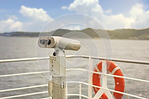 Binocular tourism telescope on the deck of a ferry ship with a lifeline buoy.
