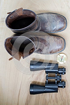 Binoculars, old boots and compass, traveler`s things, on the wooden background