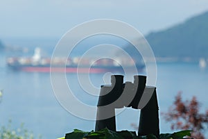 Binoculars resting on a table. Container ship cargo ship on the background. Ligurian Mediterranean sea in the Gulf of La Spezia photo