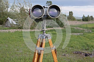 A binoculars with a tripod with a azimuth head in a forest on a sand with grass photo