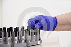 Biochemical laboratory. the technician`s hand puts a blood test tube in the stand. Close-up of a blood tube held by a gloved hand