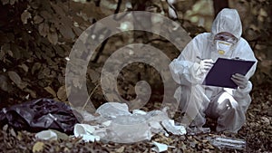 Biochemist in protective uniform writing report checking plastic landfill forest