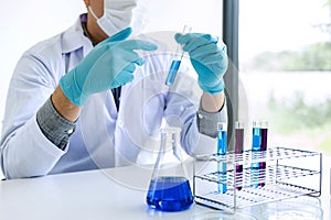 Biochemistry laboratory research, Scientist or medical in lab coat holding test tube with reagent with drop of color liquid over