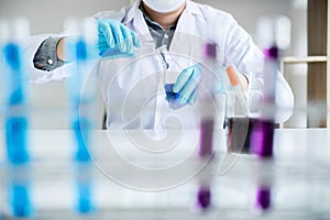 Biochemistry laboratory research, Scientist or medical in lab coat holding test tube with reagent with drop of color liquid over