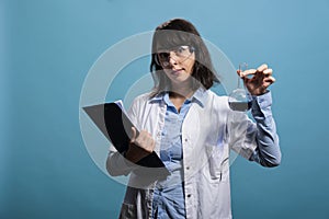 Biochemistry research specialist holding volumetric glass flask filled with blue unknown liquid substance sample.