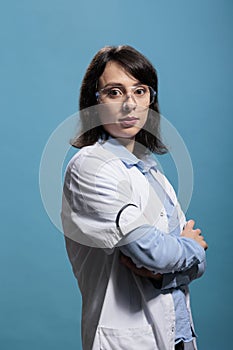 Biochemistry specialist wearing protective goggles and lab coat standing on blue background