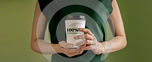 Biodegradable and Compostable Packaging Concept. Closeup of Woman Holding a Hot Cup of Coffee against a Green Wall. Zero Waste