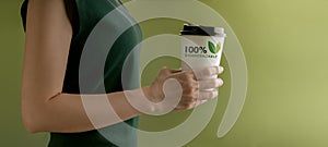 Biodegradable and Compostable Packaging Concept. Closeup of Woman Holding a Hot Cup of Coffee against a Green Wall. Zero Waste