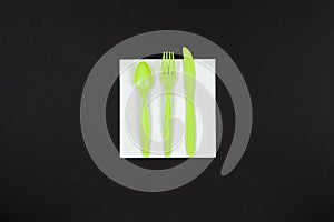 Biodegradable reusable recyclable green fork, spoon, knife made from corn starch or oats laid on white napkin on black background