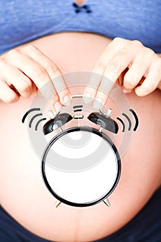 Biological clock ticking concept with pregnant woman and old clock in front of her belly