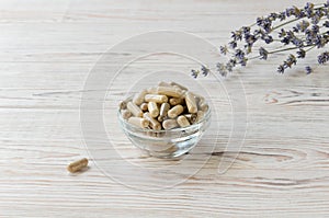 Biologically active supplement in glass bowl on white wooden background