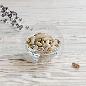 Biologically active supplement in glass bowl on white wooden background.