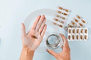 Biologically active supplements pill in hand and glass of water and blisters with other tablets on blue background