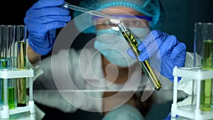 Biologist adding oily substance in tube with green plant, biofuel extraction