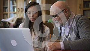 Biologist Professor and female student are talking at table with laptop in library.