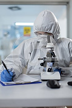 Biologist researcher wearing protective suit analyzing chemicals using medical microscope