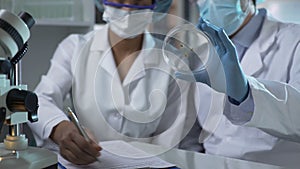 Biologist showing new organisms on lab dish, assistant filling in paper forms