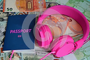 The biometric passport and pink headphones lie on the background of Euro and dollar paper money. expensive vacation, necessary