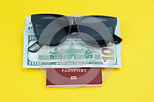 Biometric passport, stack of one hundred dollar bills and sunglasses on a yellow background