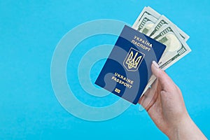 Biometric Ukrainian passport and money in a hand on a blue background isolated.