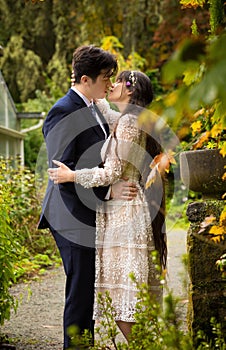 Biracial bride and groom outdoors kissing by stone wall