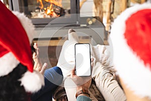 Biracial couple with santa hats having video call on smartphone at christmas at home, copy space