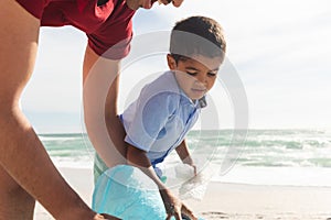 Biracial father and son collecting plastic garbage together at beach on sunny day