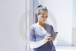 Biracial female doctor wearing scrubs using smartphon in hospital, copy space