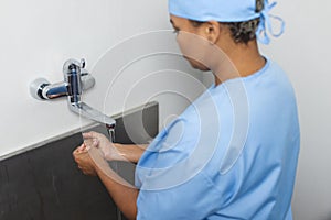 Biracial female doctor wearing scrubs washing hands in operating theatre