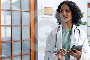 Biracial female doctor wearing sthethoscope, using smartphone at doctor\'s office photo