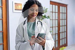 Biracial female doctor wearing sthethoscope, using smartphone at doctor\'s office photo