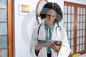 Biracial female doctor wearing sthethoscope, using tablet at doctor\'s office