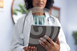 Biracial female doctor wearing sthethoscope, using tablet at doctor\'s office