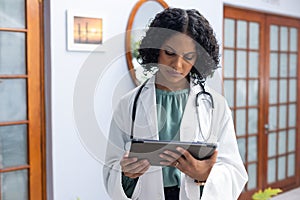 Biracial female doctor wearing sthethoscope, using tablet at doctor\'s office photo