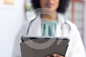 Biracial female doctor wearing sthethoscope, using tablet at doctor's office