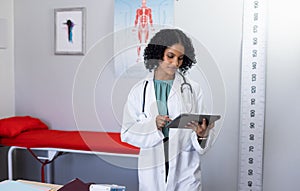 Biracial female doctor wearing sthethoscope, using tablet at doctor\'s office photo