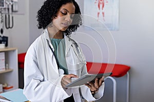 Biracial female doctor wearing sthethoscope, using tablet at doctor's office photo
