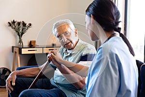 Biracial female physiotherapist consoling caucasian senior man sitting with walking cane on sofa