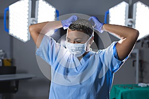 Biracial female surgeon wearing scrubs and face mask in operating theatre