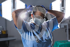 Biracial female surgeon wearing scrubs and face mask in operating theatre