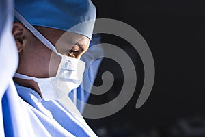 Biracial female surgeon wearing surgical gown and face mask in operating theatre, copy space