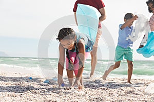 Biracial girl collecting plastic garbage on sand at beach with family during sunny day